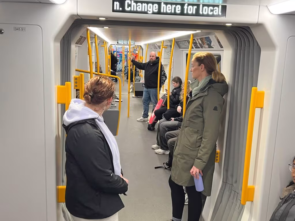 Image shows people sitting and standing on a Metro train